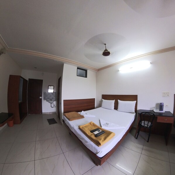 Habitación de hotel con cama, escritorio, silla, ventilador de techo, una ventana pequeña y lavamanos.