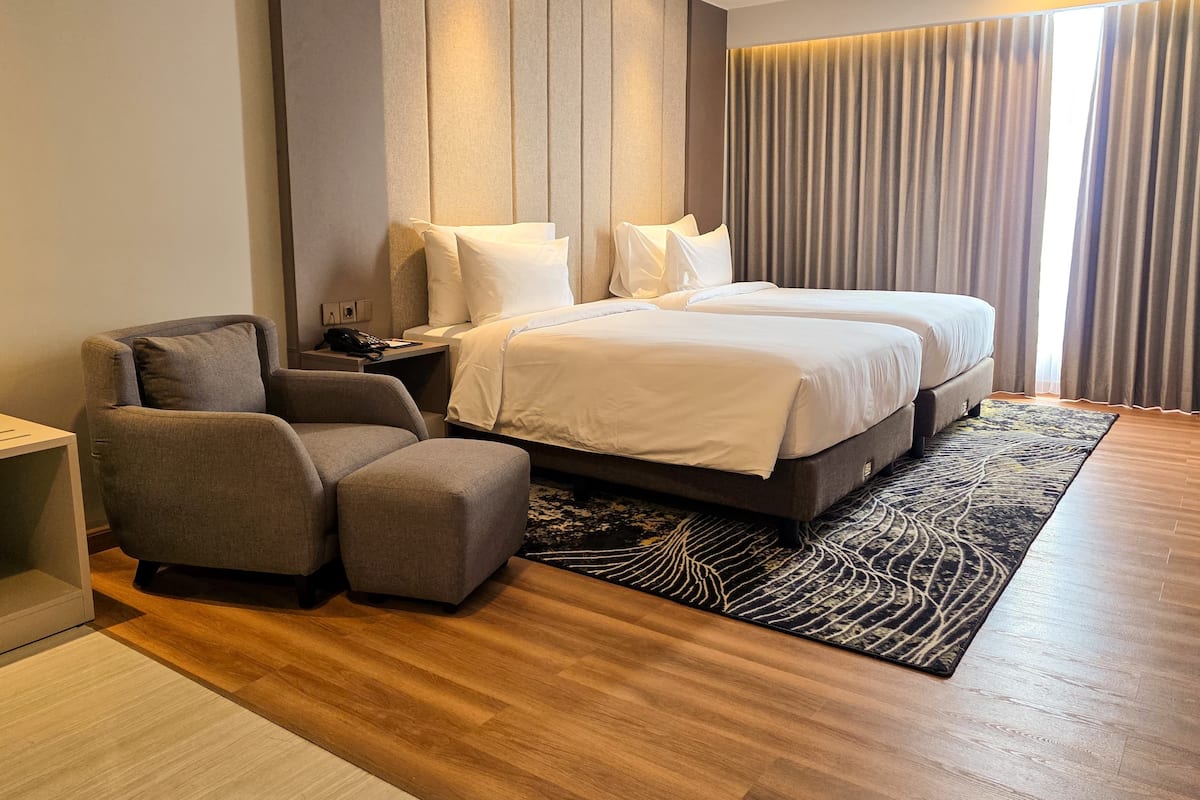 A modern hotel room with a large bed, two bedside tables, a chair, and a patterned rug.