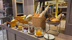 A breakfast buffet with various breads, pastries, and spreads.