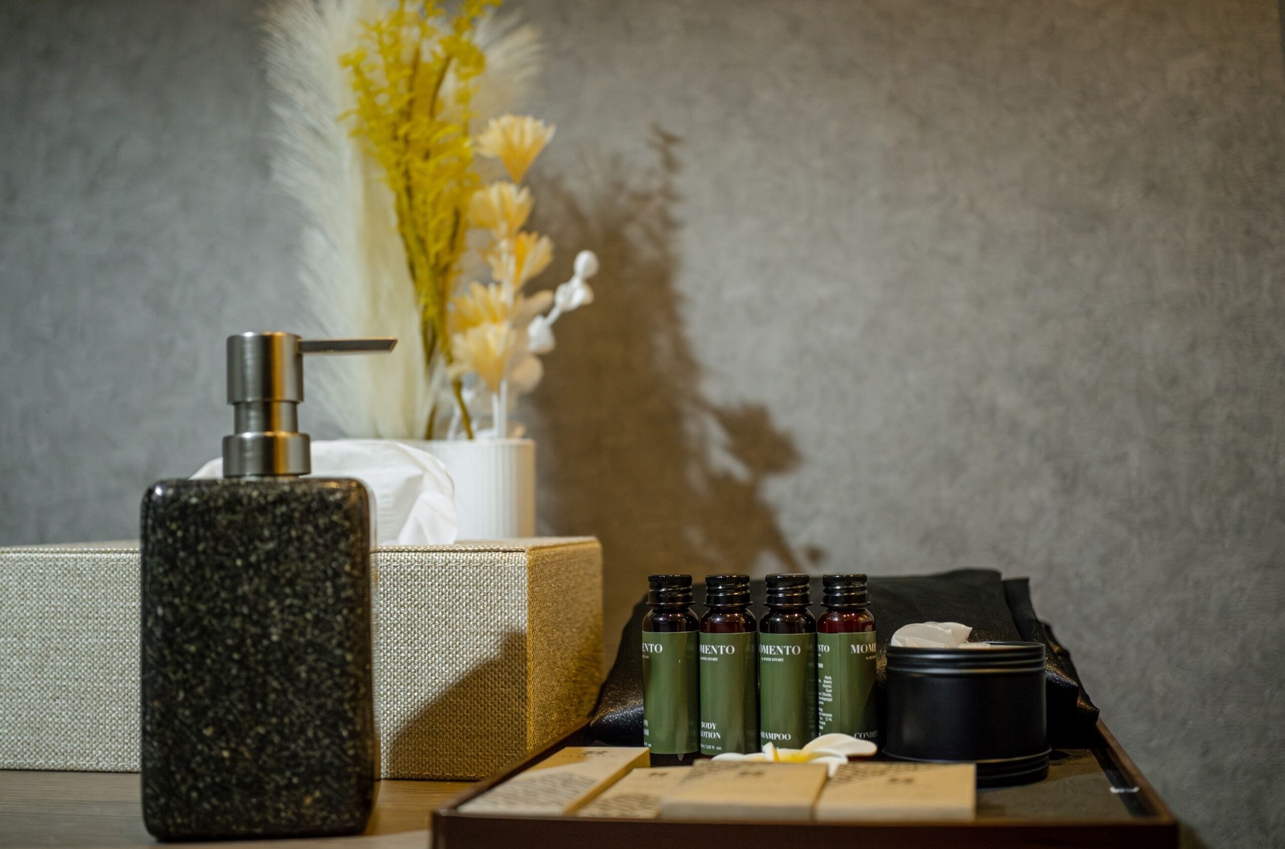A bathroom vanity with a granite soap dispenser, a white towel, and a set of toiletries including shampoo and conditioner bottles.