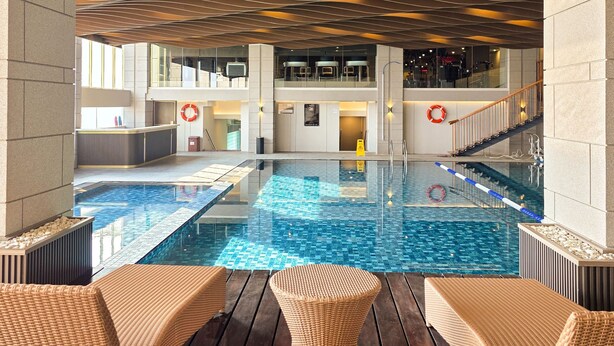 A pool area with lounge chairs, a clear pool, and a modern ceiling design.