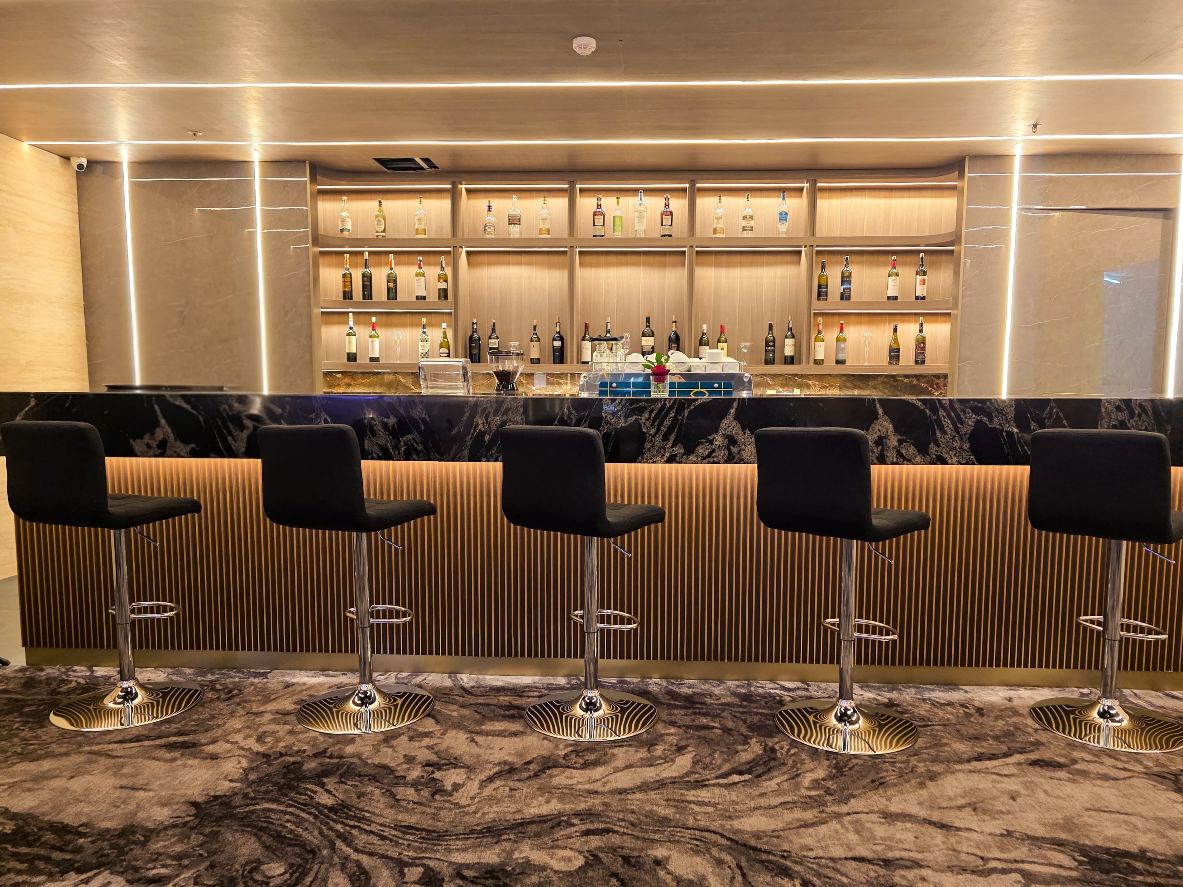 A bar area with a marble countertop, black bar stools, and shelves of liquor bottles.