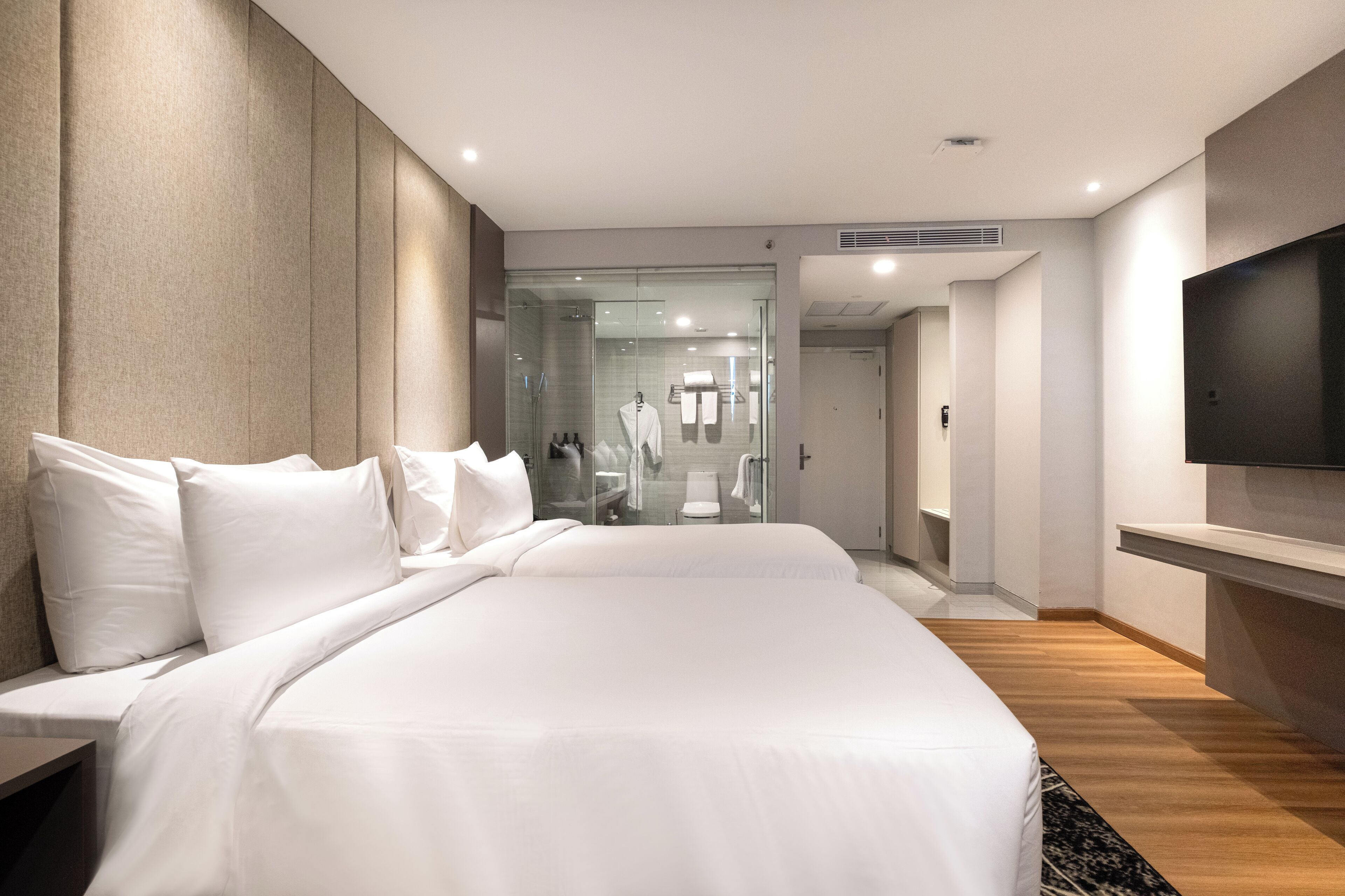 A modern hotel room with a large bed, a TV mounted on the wall, and a glass-enclosed shower area.