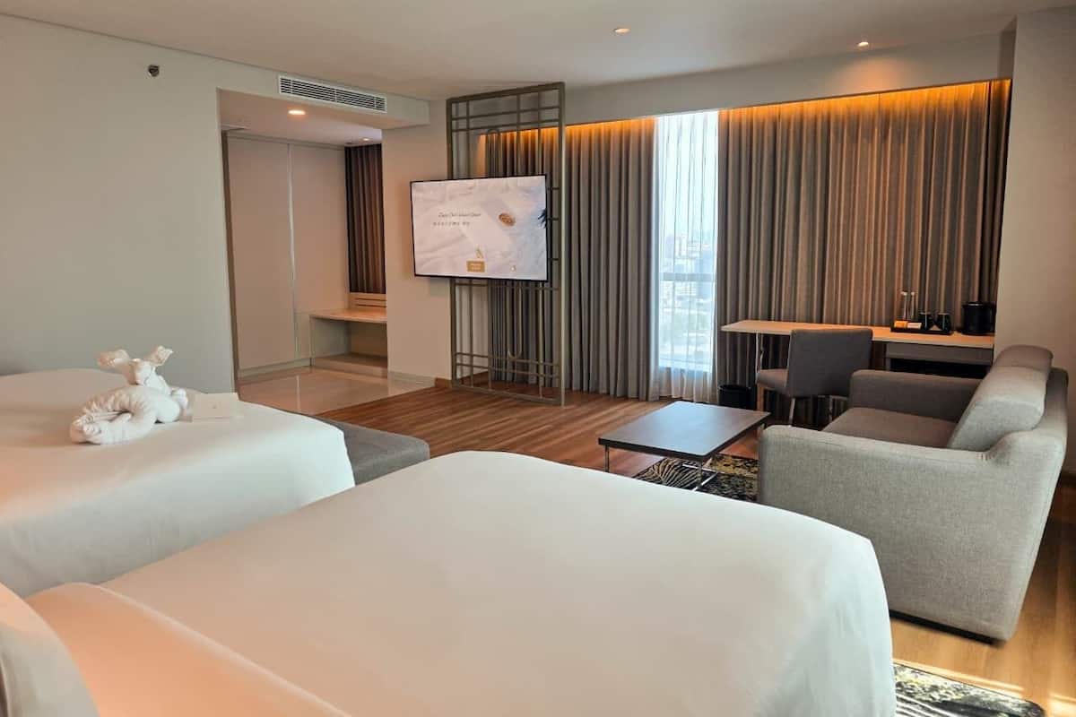 A hotel room with two beds, a desk, a sofa, and a TV.