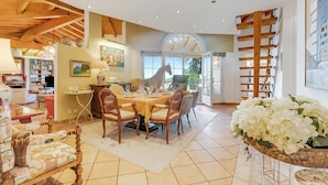 A spacious dining area with a wooden table and chairs, surrounded by bookshelves and a large window. - Villa Tre Pini Garden Escape (Lugano)