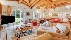 A spacious living room with a high wooden ceiling, a large TV, and a red sofa. - Villa Tre Pini Garden Escape (Lugano)