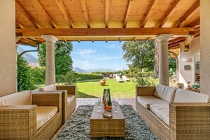 A covered outdoor seating area with wicker furniture and a table with a vase and glasses. - Villa Tre Pini Garden Escape (Lugano)