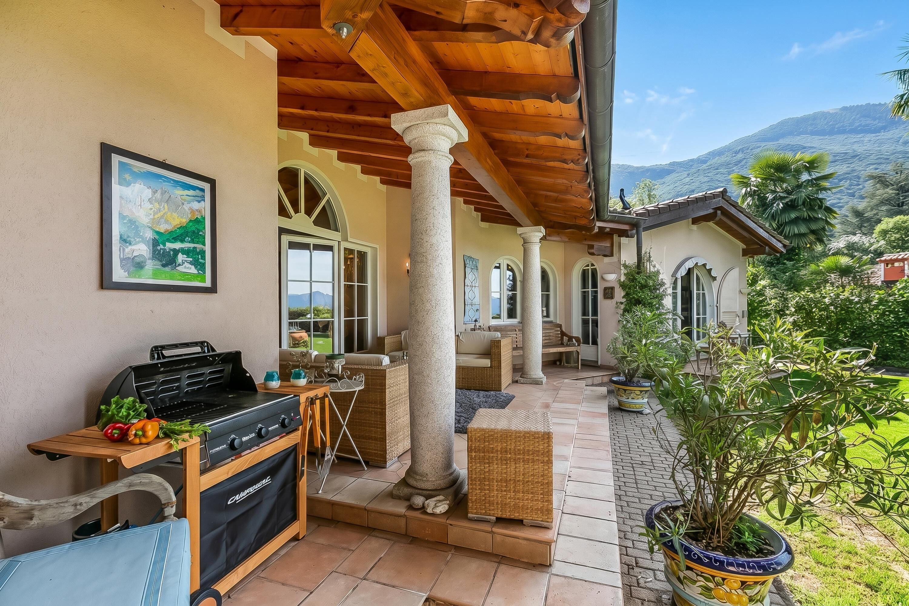 An outdoor patio with a grill, wicker furniture, and potted plants.