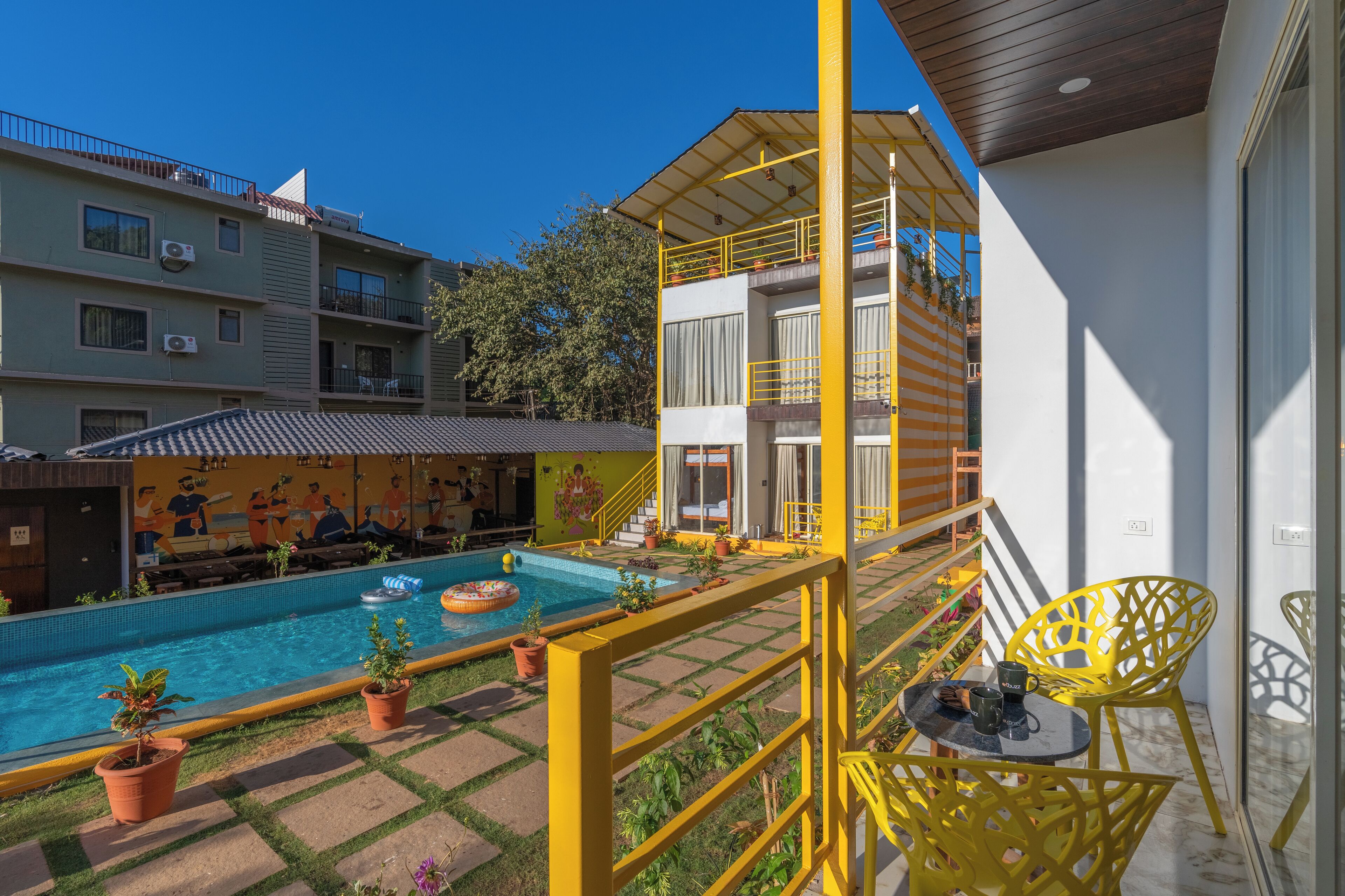 Un área de piscina con una piscina azul cristalina, barandales amarillos y plantas en macetas.