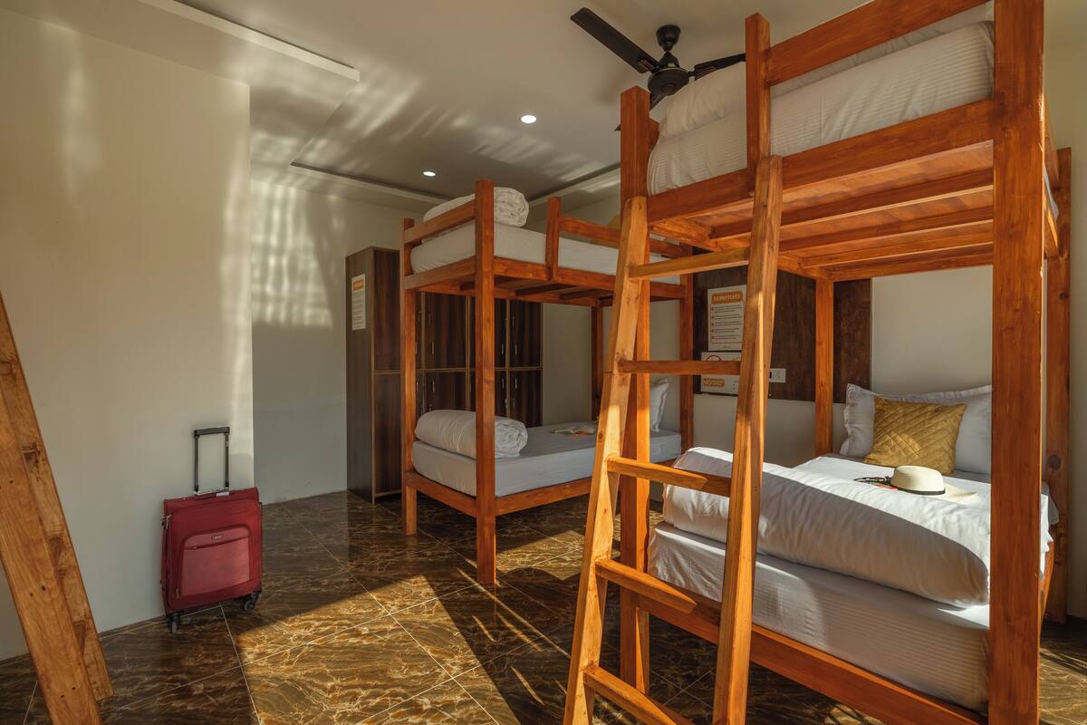 A room with three wooden bunk beds, a red suitcase, and a ceiling fan.