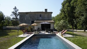 A pool with lounge chairs and umbrellas, a stone building, and trees in the background. - Gite Les Bons Amis Fronsac 100m2 - 3ch - 6pax - Piscine chauffée - jardin 1300m2 (Fronsac)