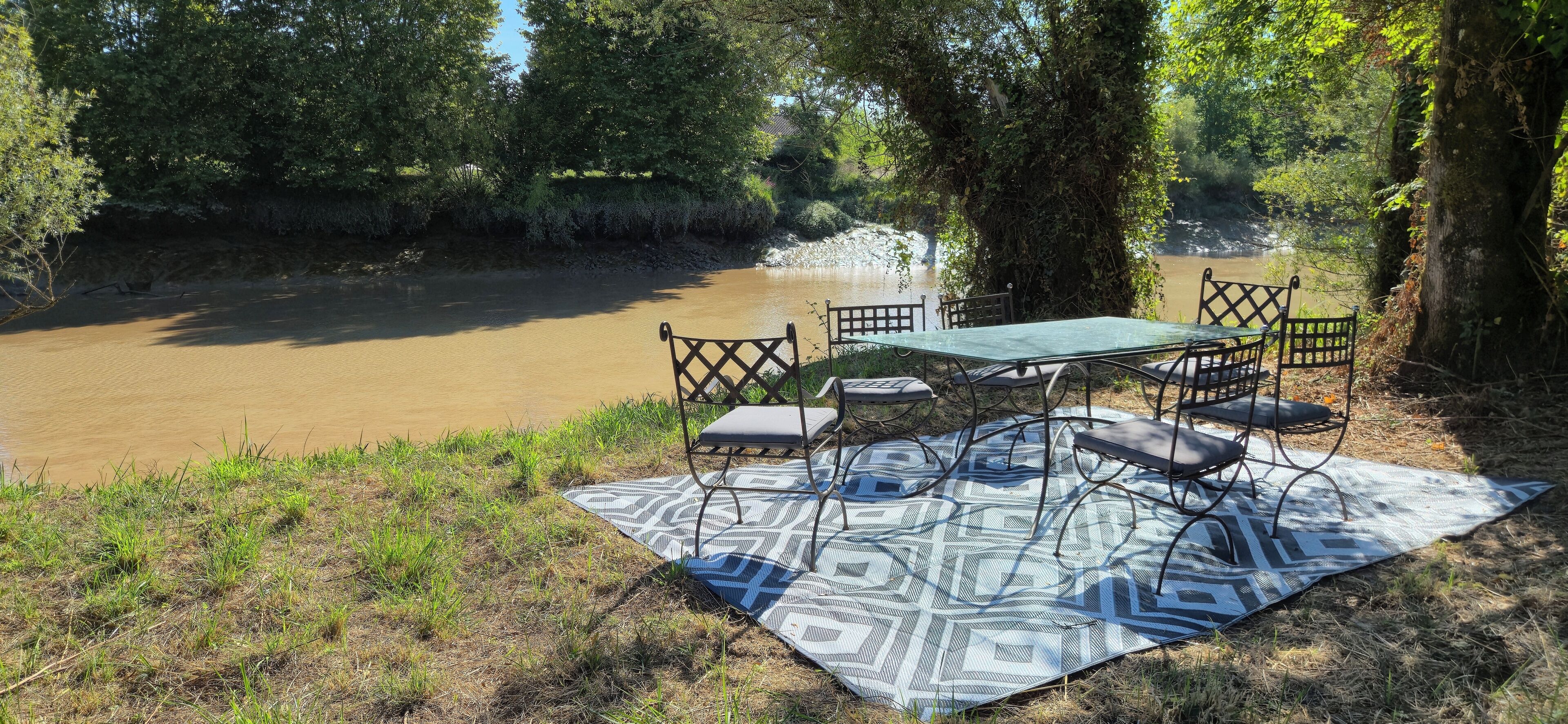 Un área de comedor al aire libre con una mesa y sillas sobre un tapete estampado, con vistas a un río.