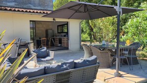 A patio with wicker furniture, a table, and an umbrella. - Gite Les Bons Amis Fronsac 100m2 - 3ch - 6pax - Piscine chauffée - jardin 1300m2 (Fronsac)