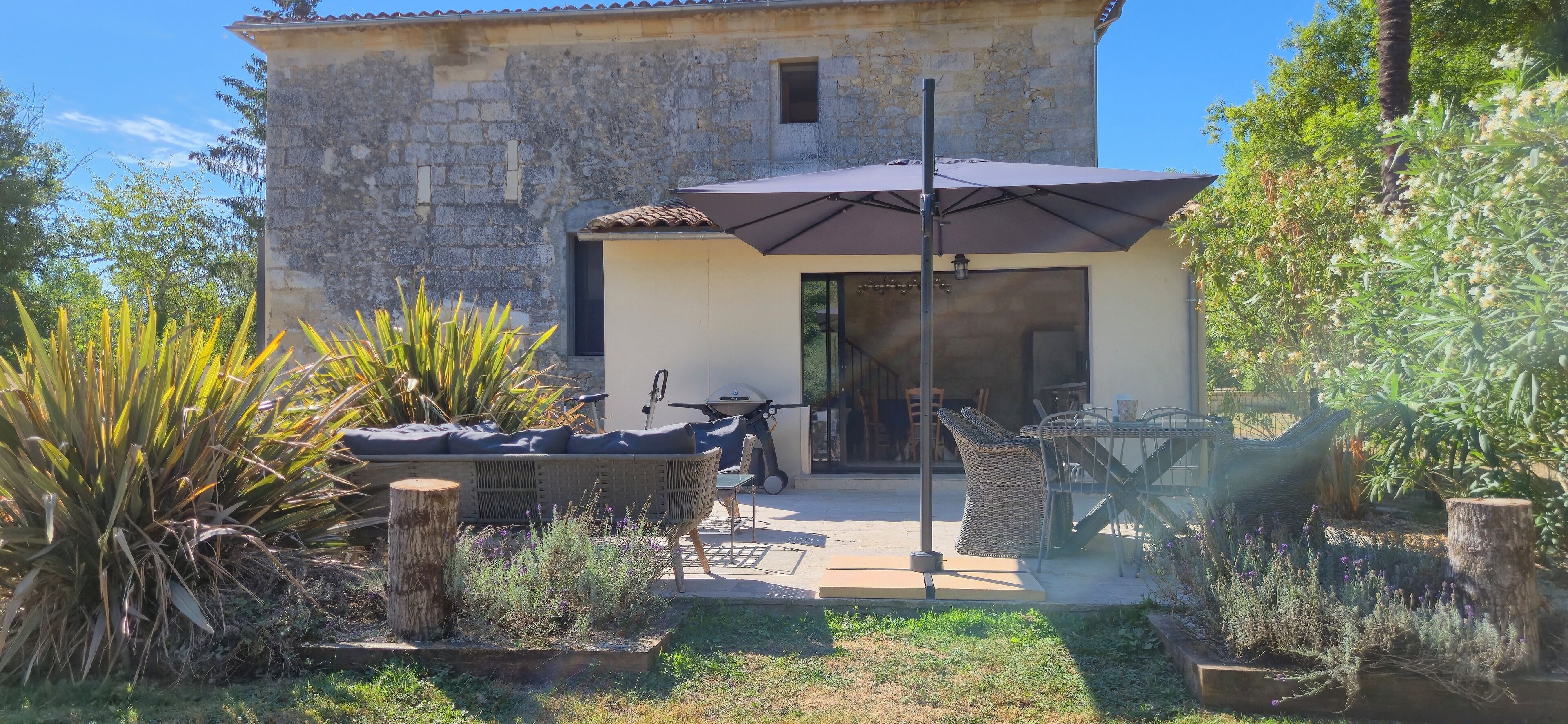 A stone building with a patio area featuring outdoor furniture, a table, and a large umbrella.