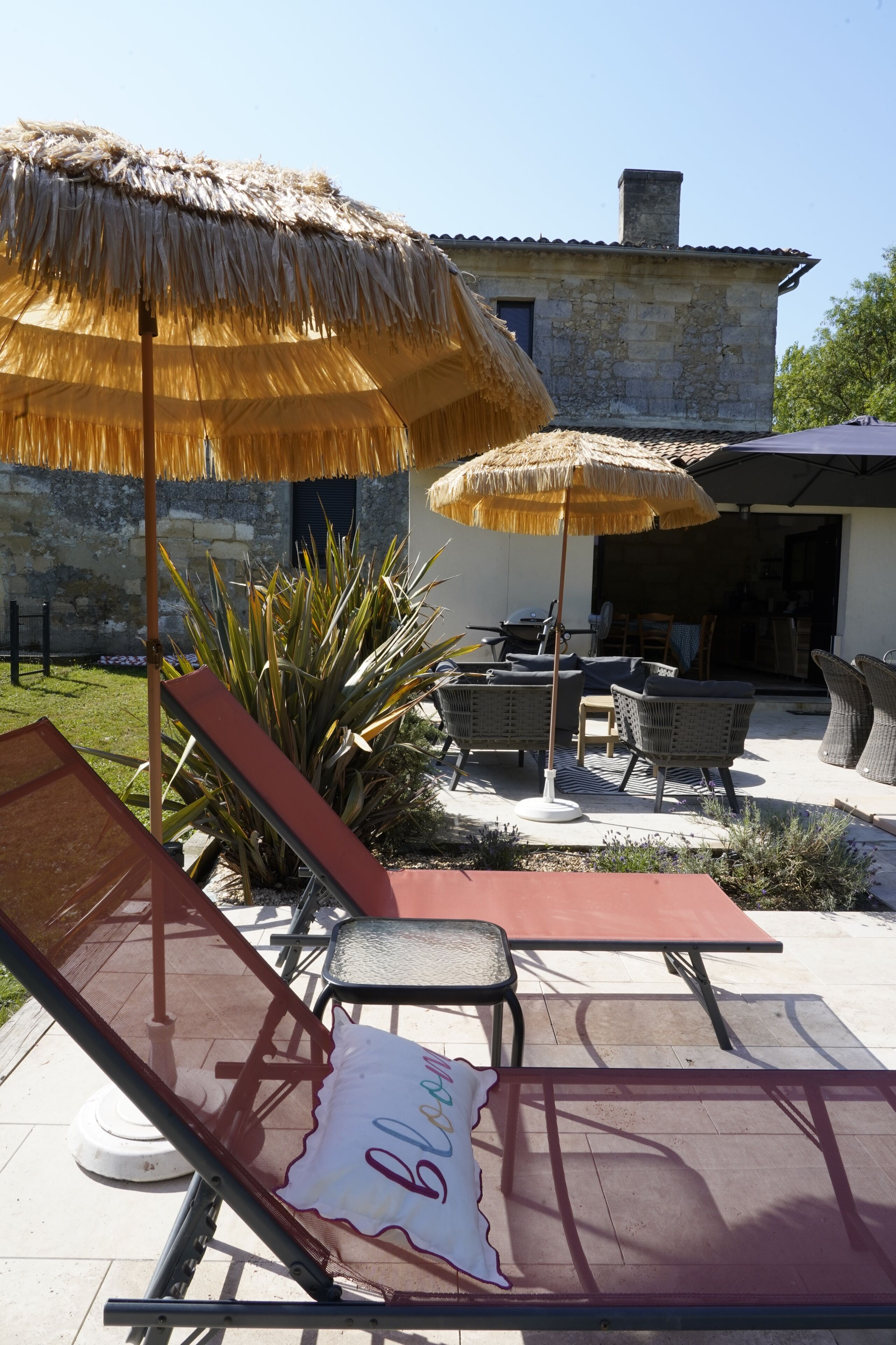 Ein Patio mit zwei Lounge-Sesseln, einem Tisch und zwei Strohdächern.