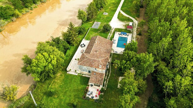 An aerial view of a house with a swimming pool, surrounded by lush greenery and a river. - Gite Les Bons Amis Fronsac 100m2 - 3ch - 6pax - Piscine chauffée - jardin 1300m2 (Fronsac)