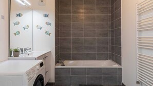 A modern bathroom with a built-in washing machine, a bathtub, and a large mirror with fish decals. - Charming Apartment  2BR/4P - Near to Lyon (Caluire-et-Cuire)