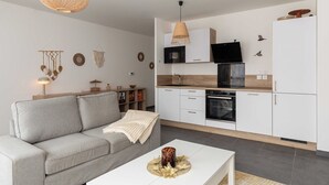 A modern kitchen with white cabinets, a microwave, and a stove. There is a grey sofa and a white coffee table with a decorative centerpiece. - Charming Apartment  2BR/4P - Near to Lyon (Caluire-et-Cuire)