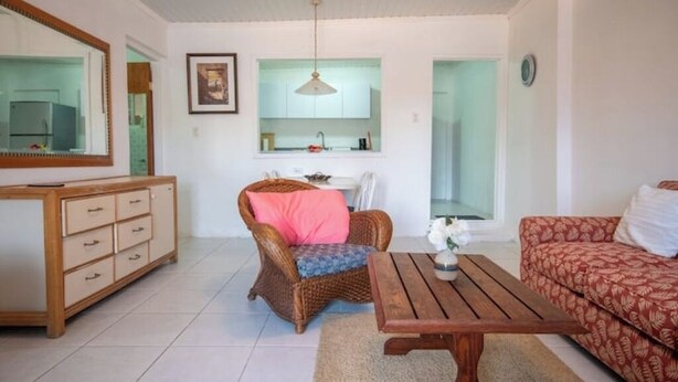 A living room with a wooden cabinet, wicker chair, wooden coffee table, and patterned sofa.