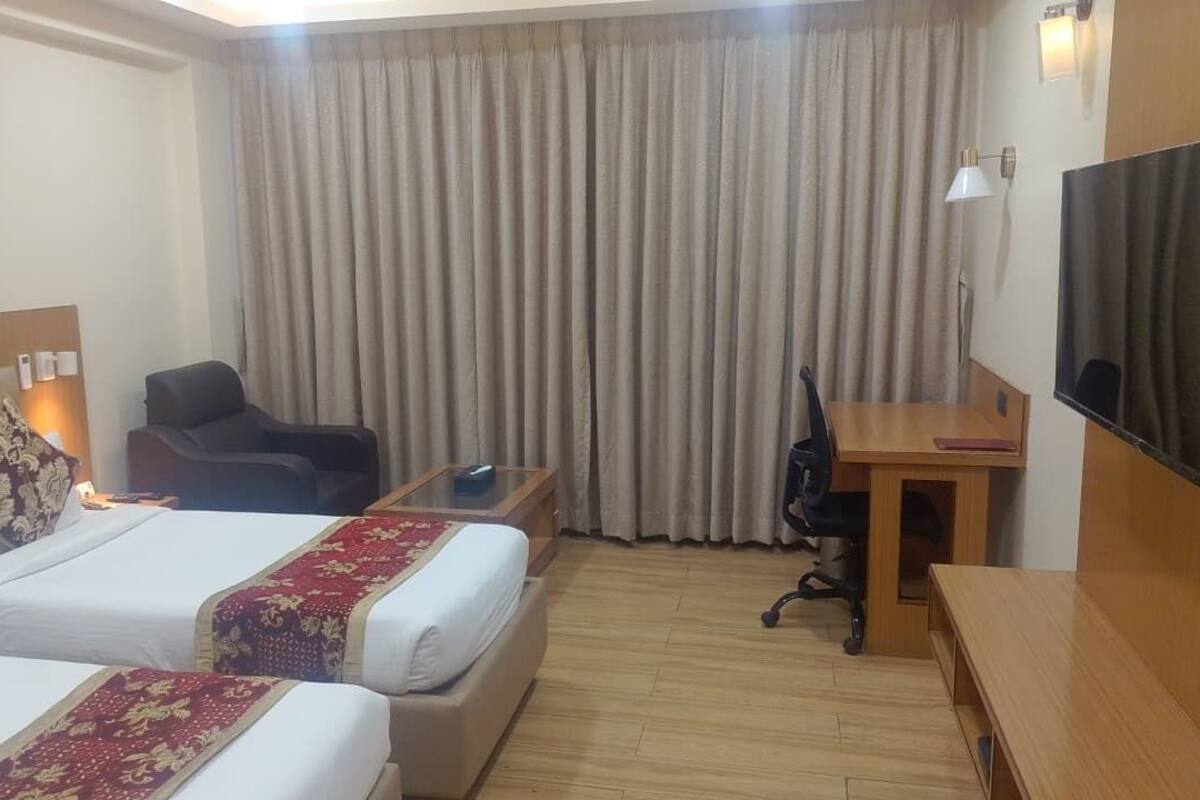 A hotel room with two beds, a desk, a chair, a television, and a large window with curtains.