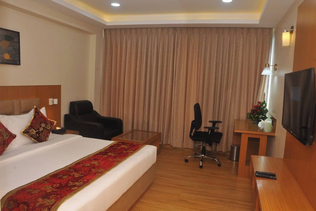 A hotel room with a bed, a desk, a chair, a television, and a large window with curtains.