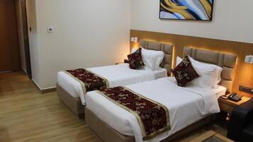A hotel room with two beds, each with a headboard and bedside tables. There is a painting on the wall above the beds.