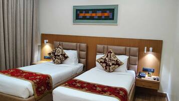Habitación de hotel con dos camas, cada una con cubrecama rojo y dorado, cabeceros de madera y mesitas de noche con teléfono y controles remotos.