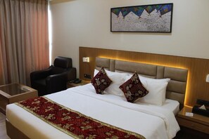 A hotel room with a bed, a chair, a nightstand, and a painting on the wall. - Hotel SR Continental (Gulbarga)