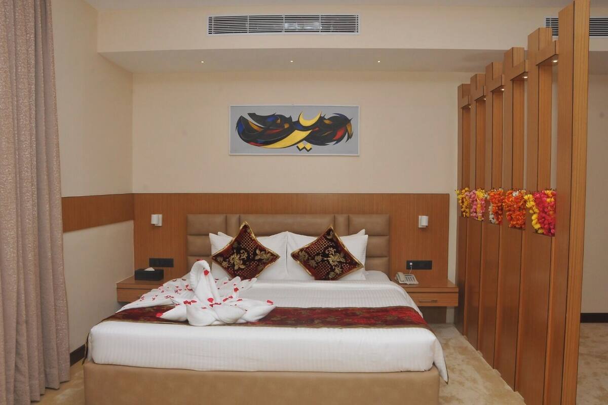 A hotel room with a bed, two nightstands, a wall-mounted artwork, and a wooden partition with flowers.