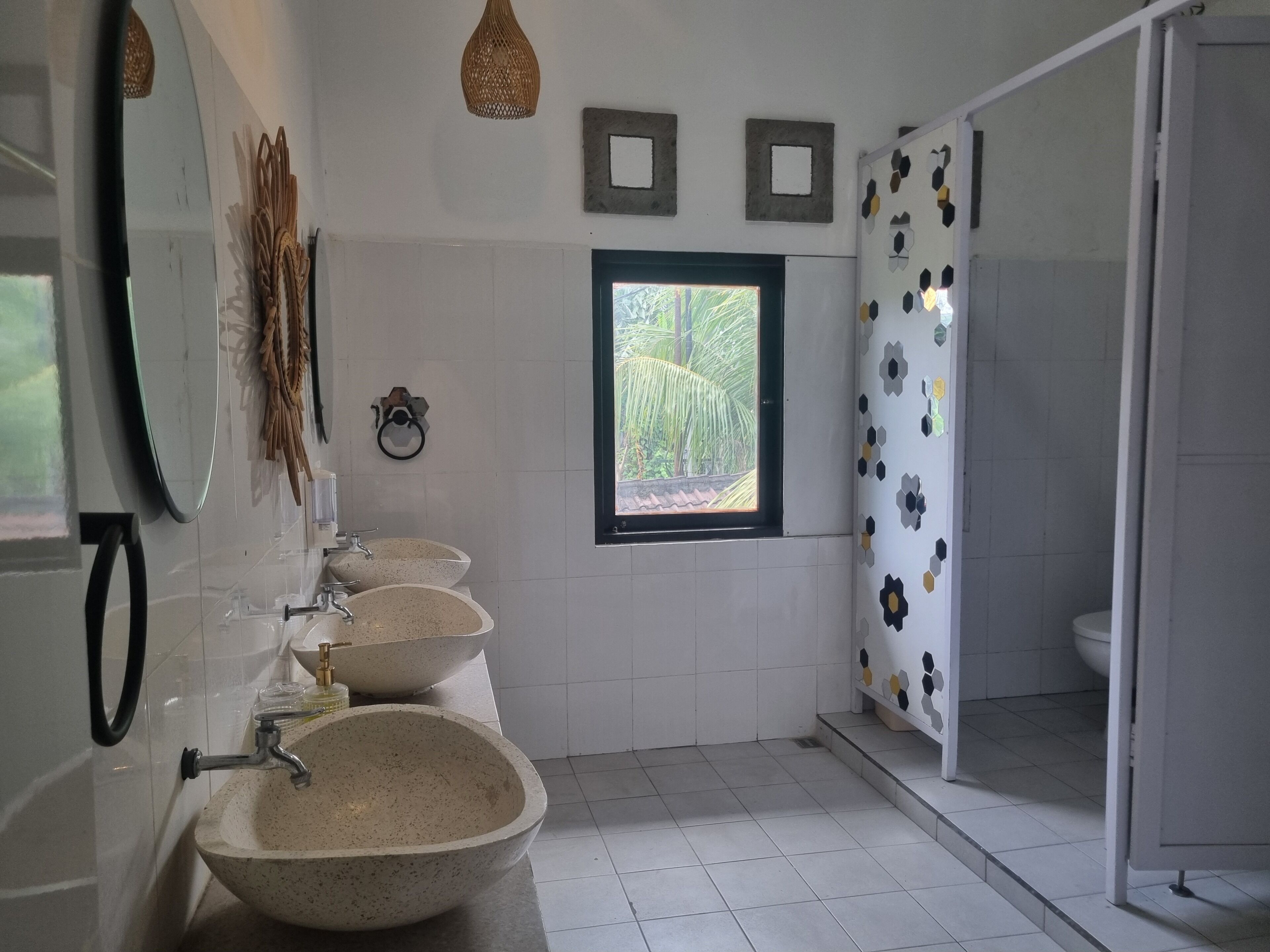Un bagno con un'ampia finestra, una doccia con motivo geometrico e un lavandino dal design originale.