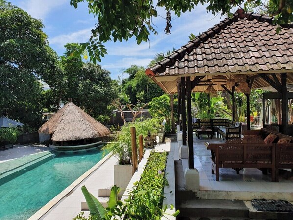A poolside area with a thatched-roof structure, wooden lounge chairs, and a covered seating area. - Glam Canggu (Canggu)