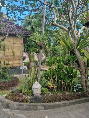 A garden with a Buddha statue, various plants, and a building with a tiled roof. - Glam Canggu (Canggu)