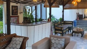 A spacious indoor area with wicker hanging lamps, a wooden bench, and a bar area with a counter and plants. - Glam Canggu (Canggu)