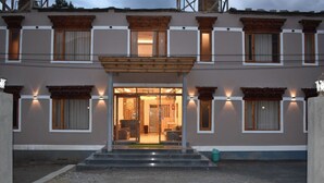 Entrada de hotel com varanda coberta, várias janelas e interior visível com assentos.