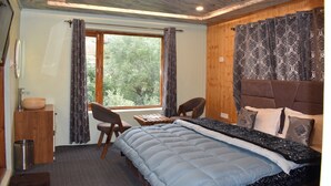 Quarto com cama, escrivaninha e cadeira. Tem uma janela com cortinas, cabeceira de madeira e um pequeno armário com uma tigela.
