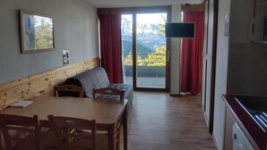 A room with a wooden dining table, a sofa, and a large window with a view of mountains. - Modern Mountain Apartment with Balcony (Chamrousse)