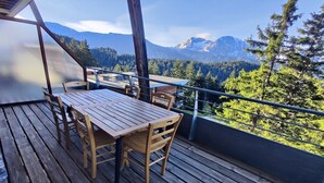 A wooden deck with a table and chairs, overlooking a mountainous landscape with trees and a clear sky. - Modern Mountain Apartment with Balcony (Chamrousse)