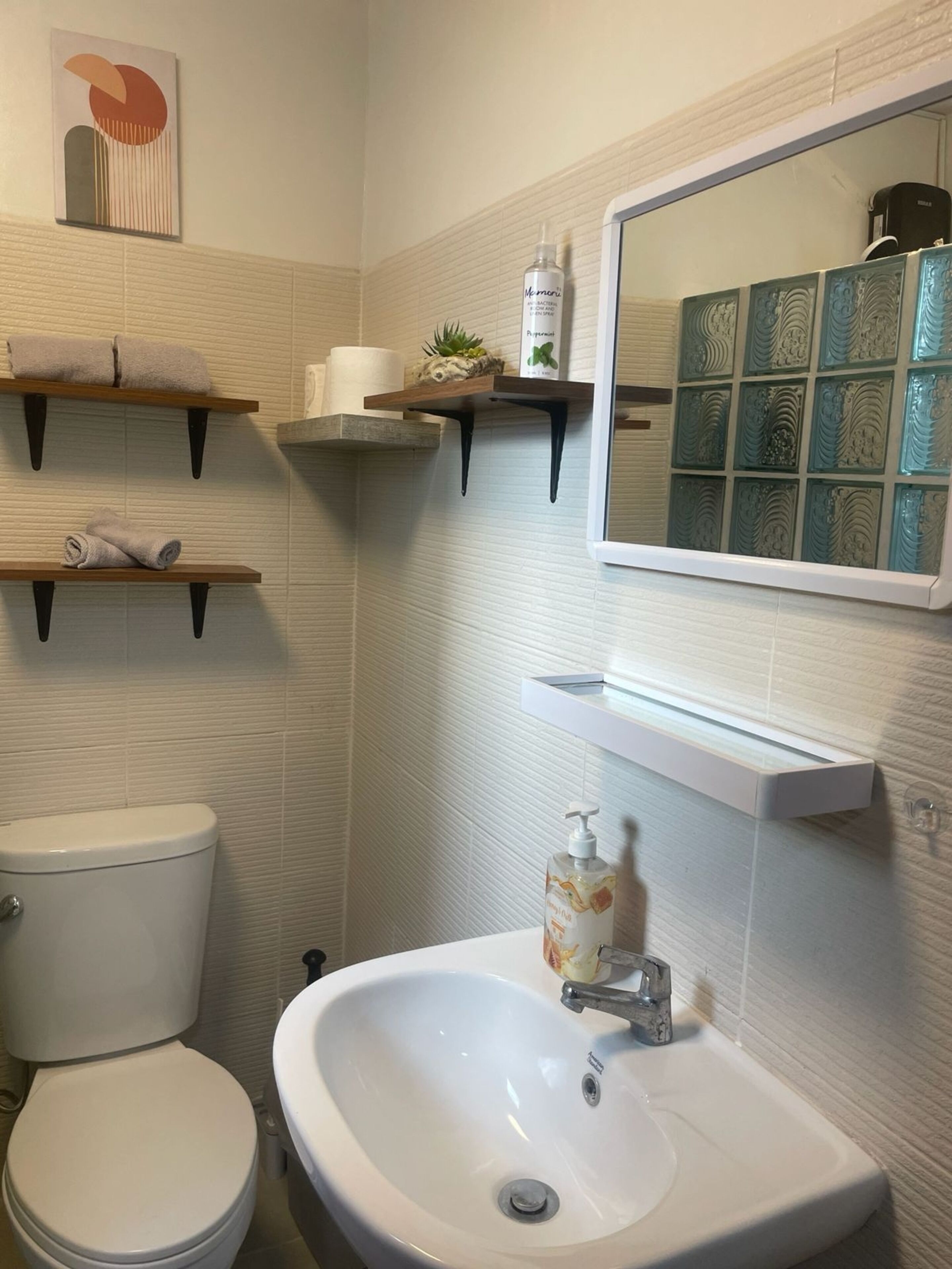 A bathroom with a toilet, a sink, and two shelves with towels and toiletries.