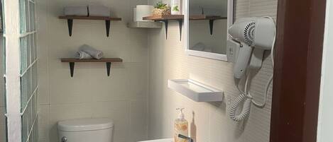 Un baño con inodoro, lavabo y secador de pelo en la pared. Hay repisas sobre el lavabo.