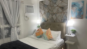 Une chambre bien rangée, avec un lit, des tables de chevet, une lampe et un climatiseur fixé au mur.