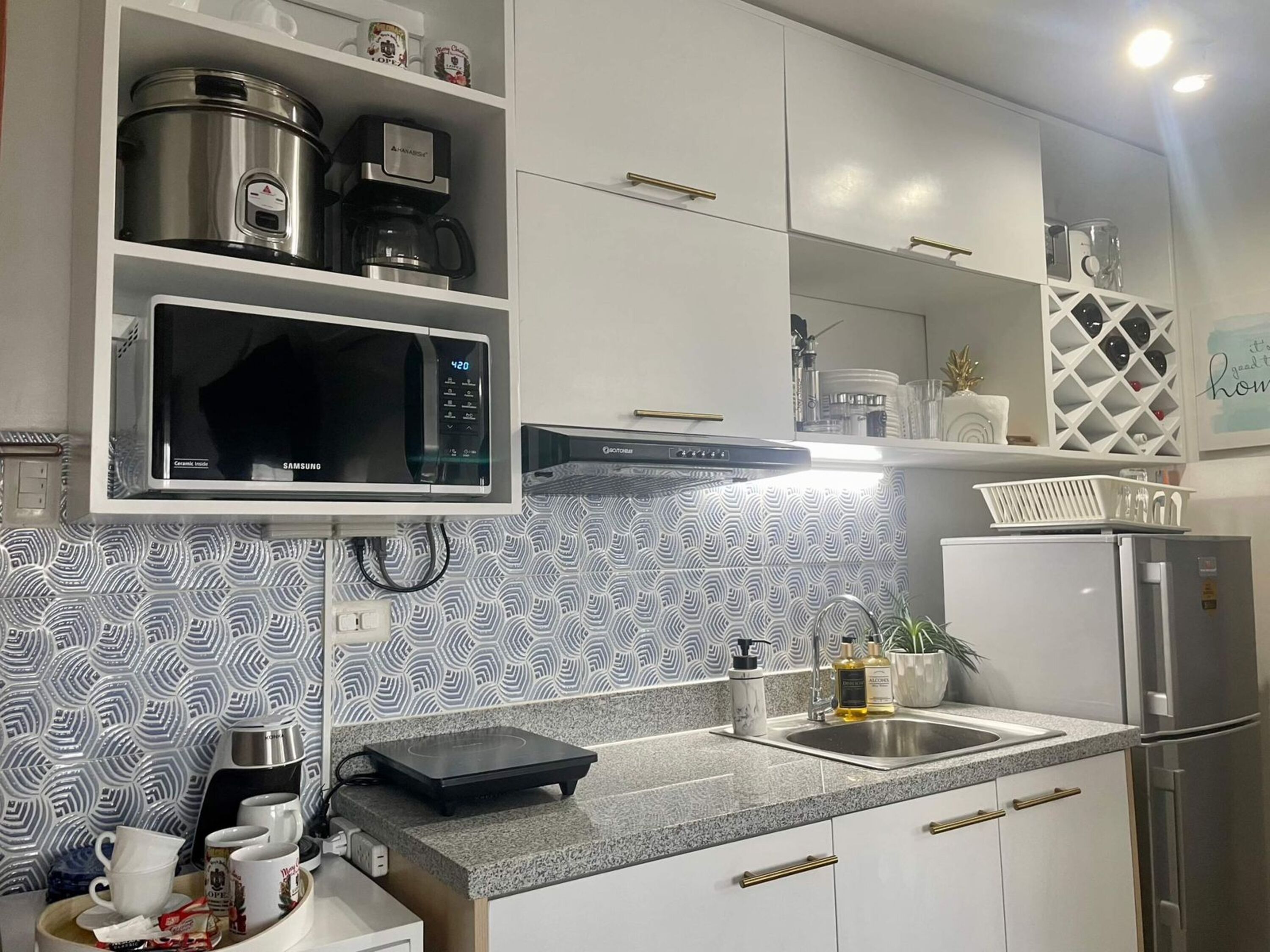Cozinha com armários brancos, micro-ondas, cafeteira e geladeira de aço inoxidável.