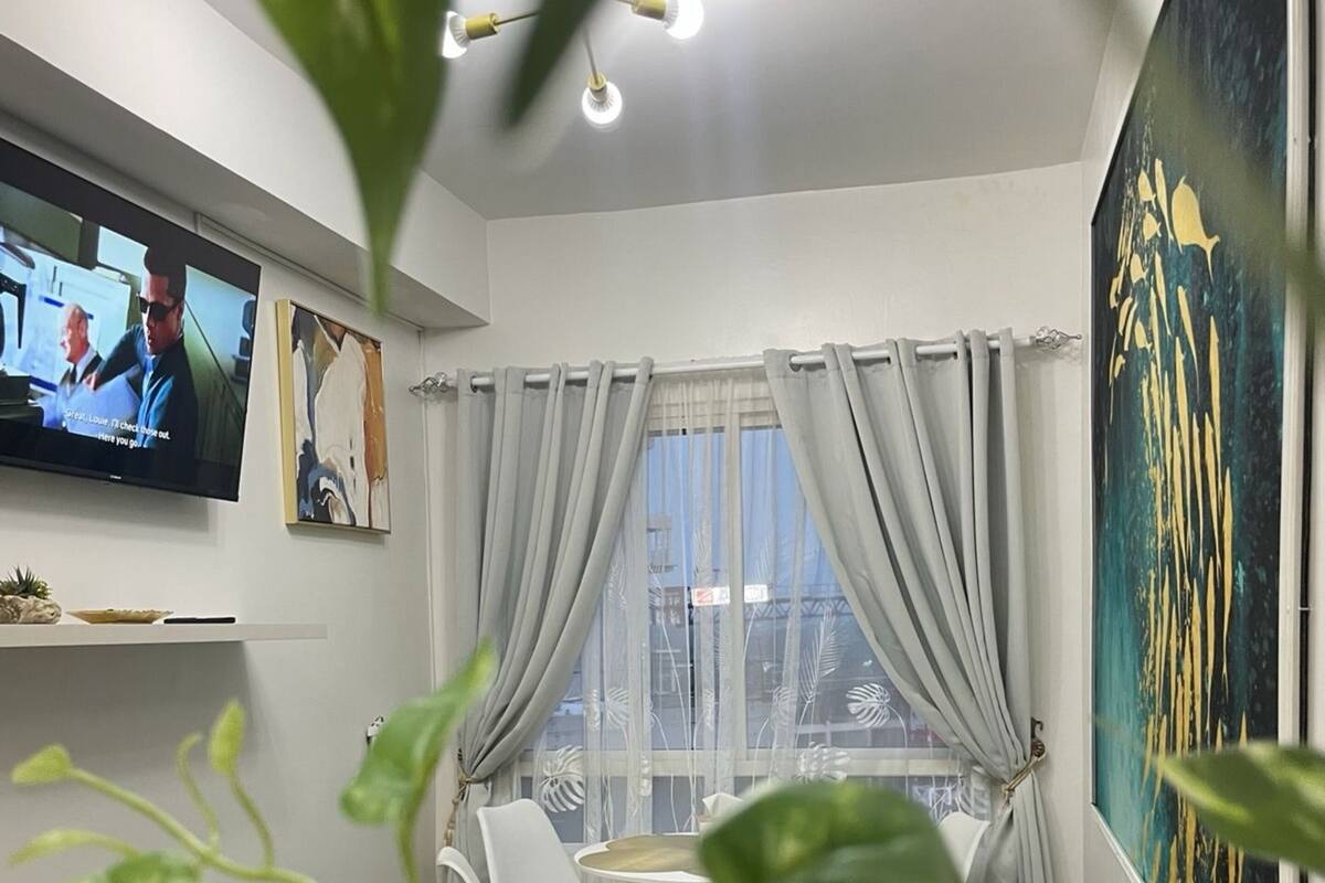 A modern living room with a TV, white chairs, a grey sofa, and a large painting.
