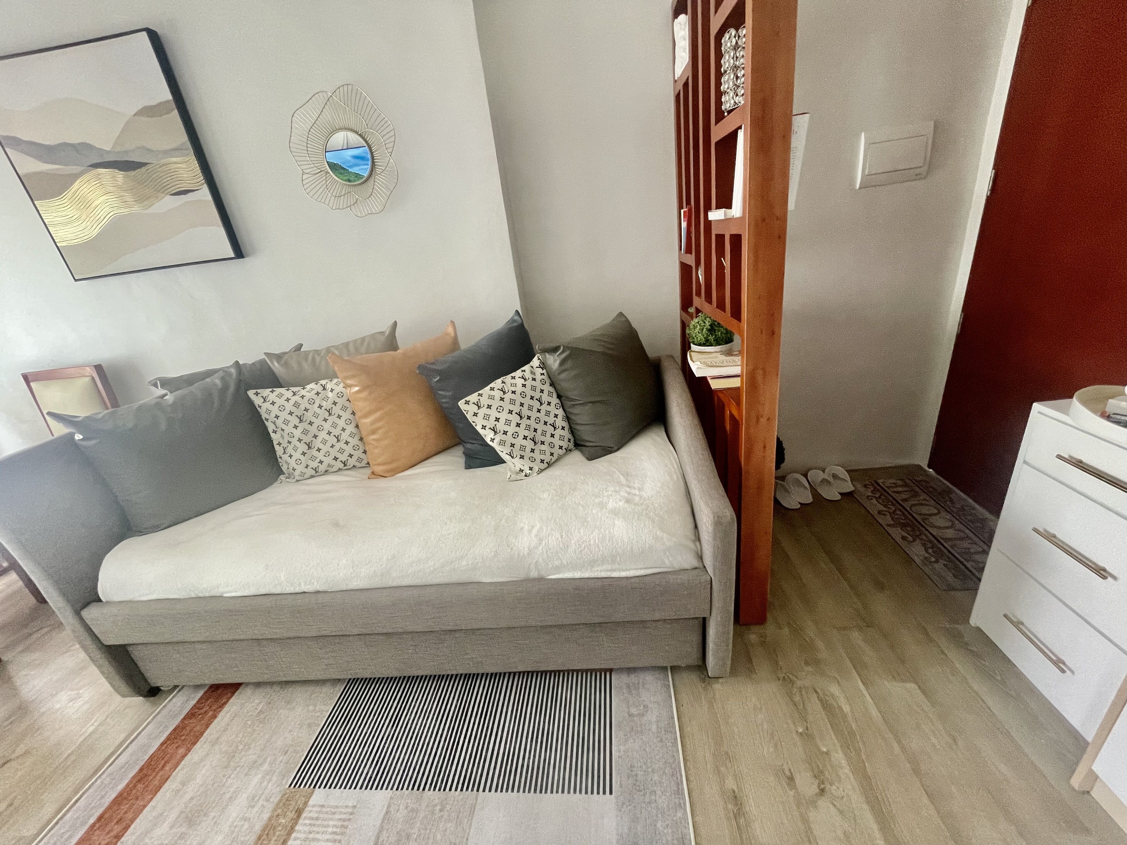 A modern living room with a sofa, patterned cushions, a decorative wall piece, and a small wooden cabinet.