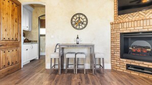 A kitchen with wooden cabinets, a dining table with two chairs, a clock on the wall, and a fireplace. - Sleeps 8, 2 Homes | Vineyard Views, Patios in Temecula Wine Trail (Temecula)