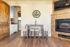 A kitchen with wooden cabinets, a dining table with two chairs, a clock on the wall, and a fireplace. - Sleeps 8, 2 Homes | Vineyard Views, Patios in Temecula Wine Trail (Temecula)