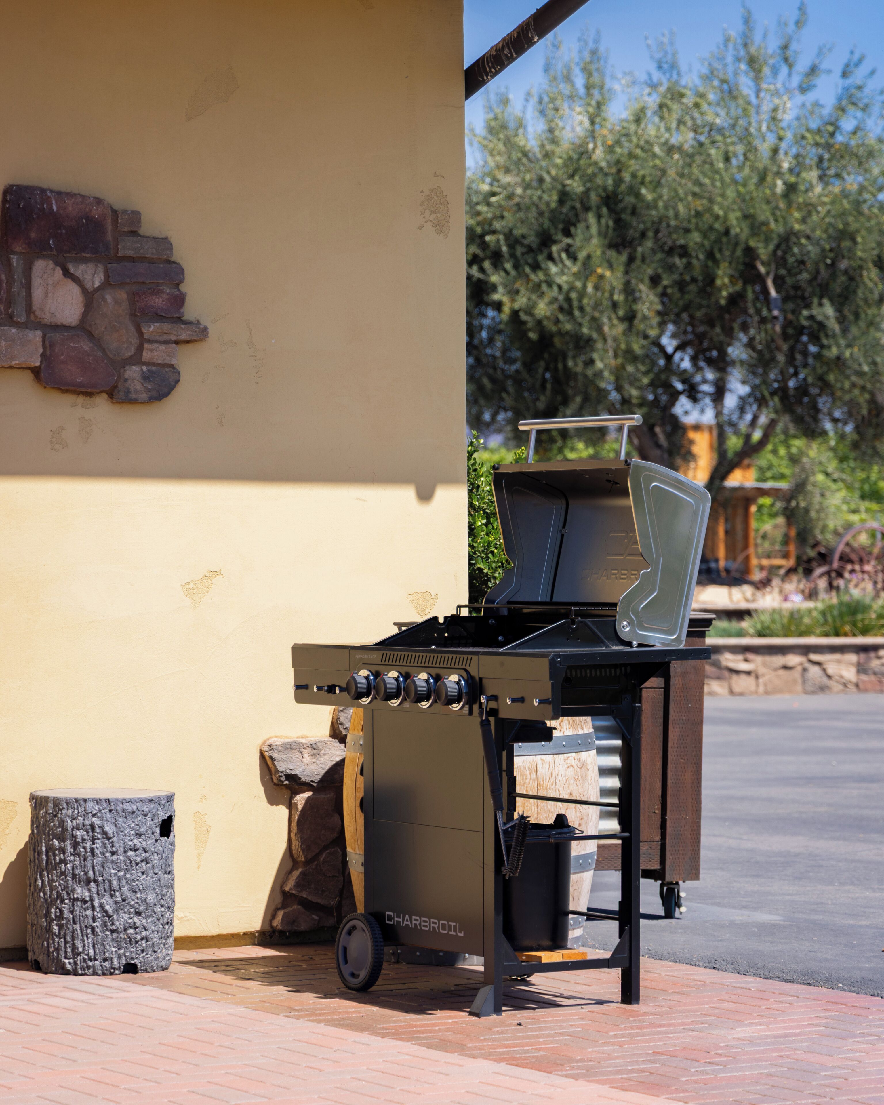 A charcoal grill with wheels, a stone wall, and a clear sky in the background.