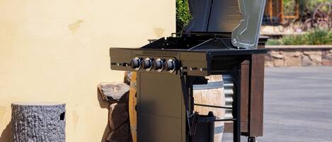 A charcoal grill with wheels, a stone wall, and a clear sky in the background.