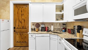 A kitchen with white cabinets, a wooden door, a dishwasher, a stove, and various appliances. - New-Build Temecula Villa with King Suite, Patio & Vineyard Views | The Villa (Temecula)