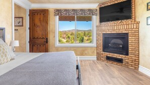 A bedroom with a large window, a fireplace, and a television mounted on the wall. - New-Build Temecula Villa with King Suite, Patio & Vineyard Views | The Villa (Temecula)