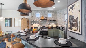 A modern kitchen with a central island, pendant lighting, and a large artwork on the wall. - Designer Desert Oasis w/ Pool, Hot Tub, Outdoor Lounge | The Riley by AvantStay (Indio)